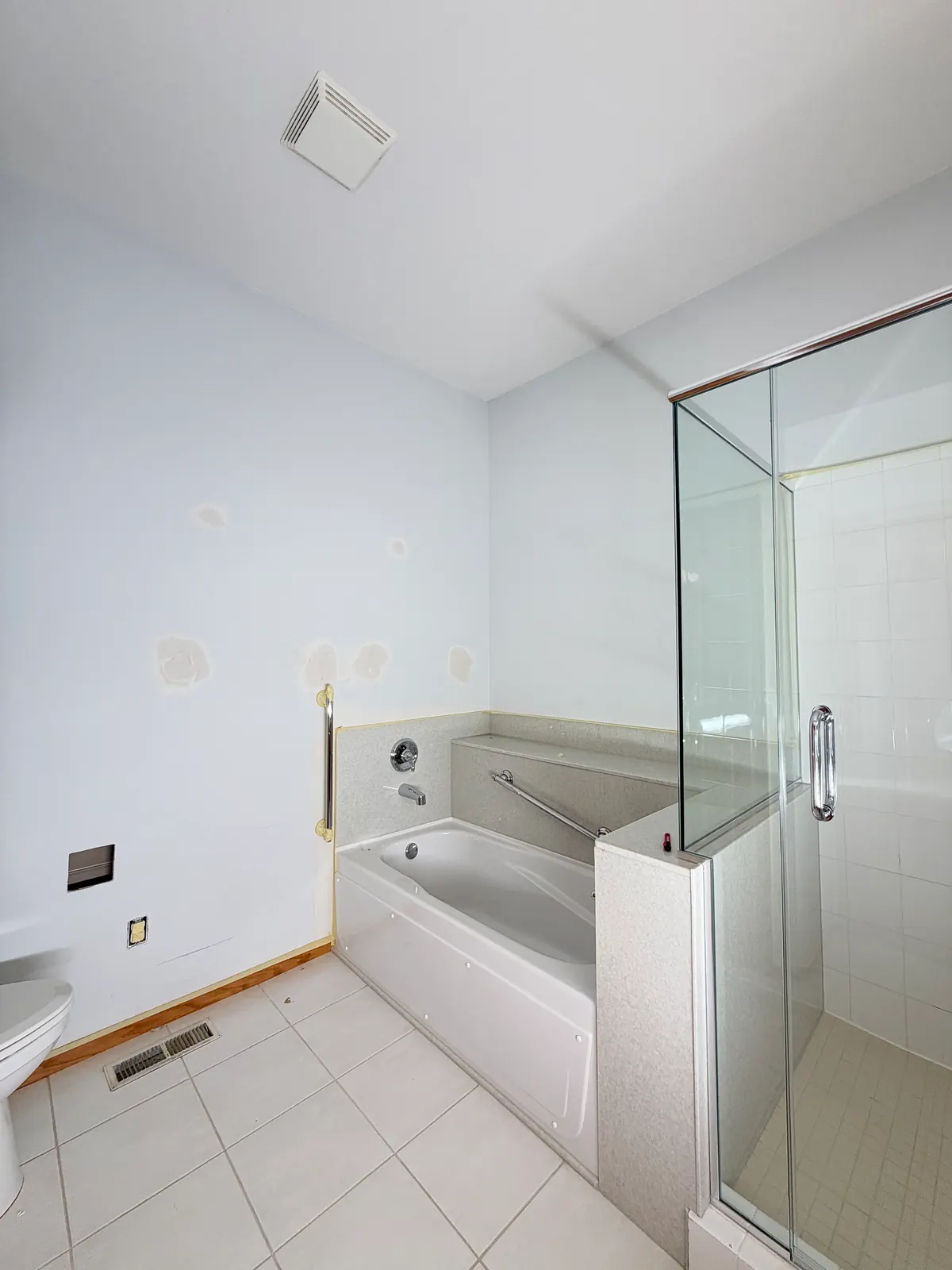 Anoka townhome primary bathroom tub wall before painting, with drywall patches spotted across the wall.
