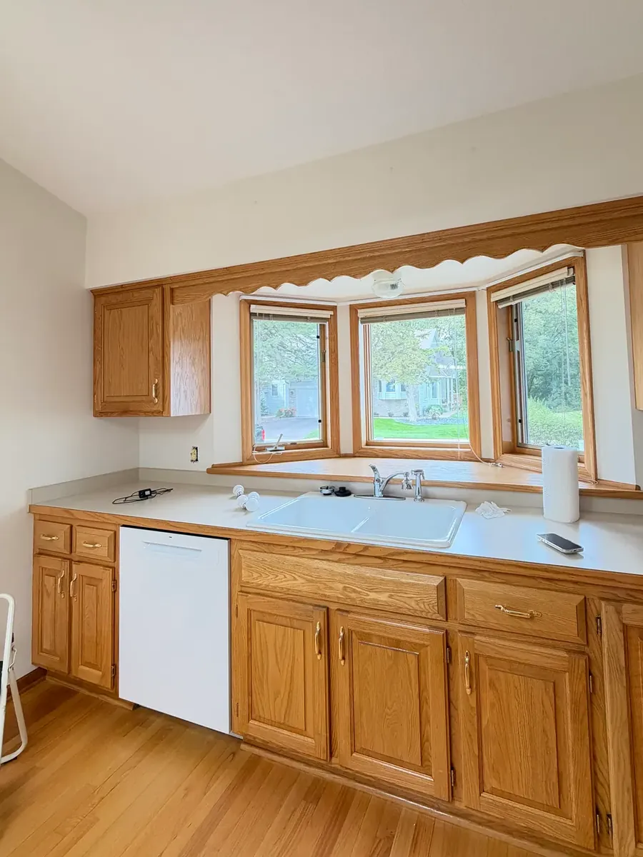 Anoka townhome kitchen before painting, white walls around the sink and bay window, oak cabinets.