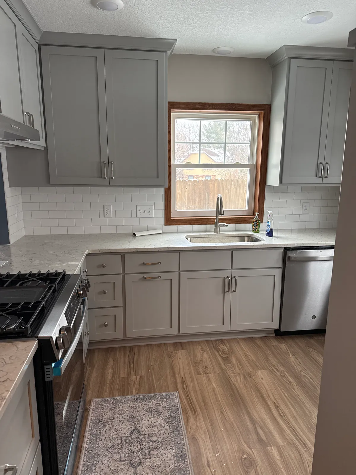 Finished Coon Rapids kitchen with gray painted cabinets along the sink window and range wall.