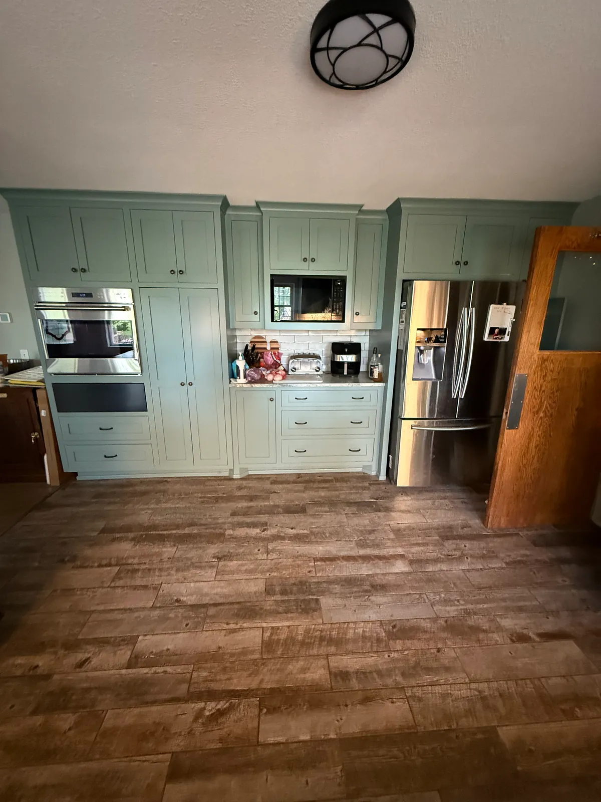 Elk River kitchen with sage green painted cabinets, after, with the tall cabinets and the built-in oven wall.