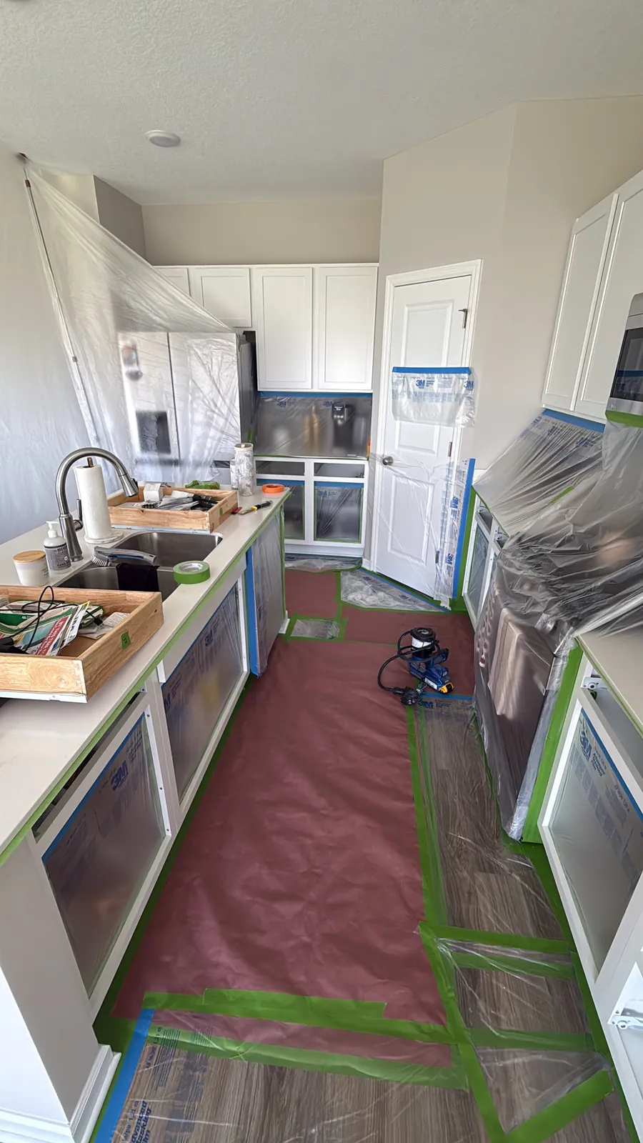 Kitchen in St. Michael sealed off with plastic, with the floor, counters, and cabinet openings masked before the cabinet boxes were sprayed.